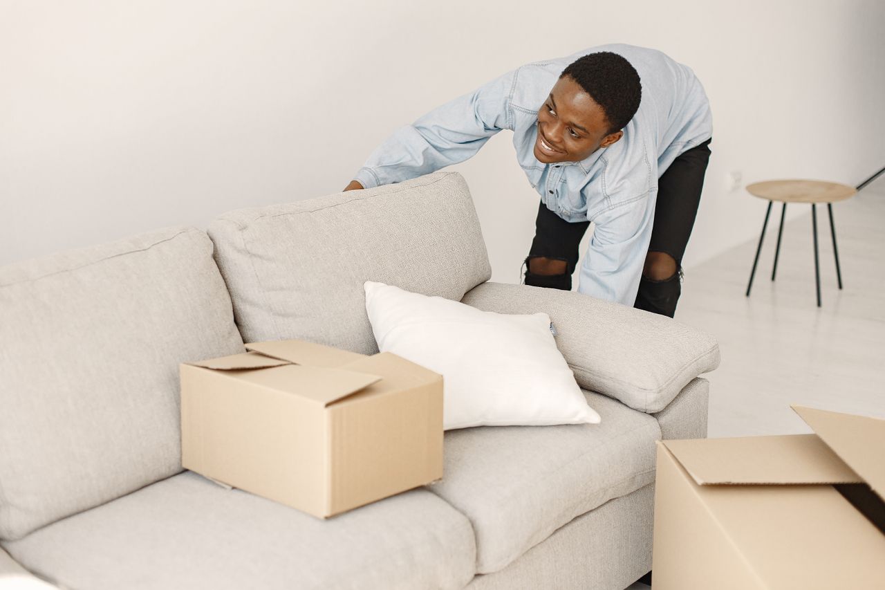 hero-01 Young man smiling while organizing cardboard boxes in a contemporary living room.